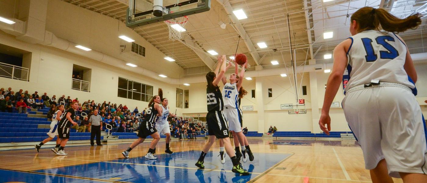 A member of the U N E women's basketball team shoots over the outstretched arms of an opponent